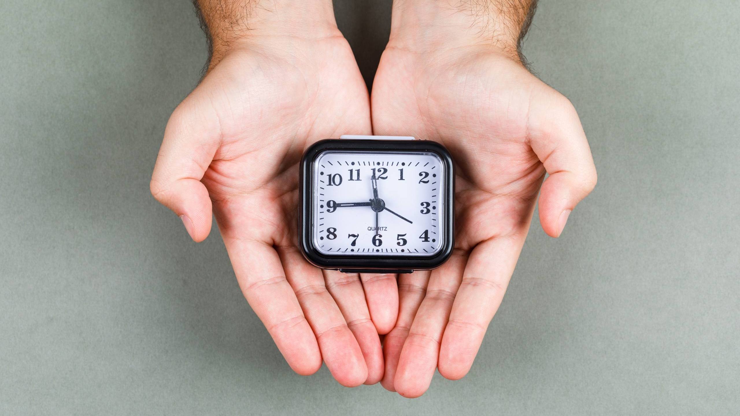 time management clock ticking concept with clock gray background top view hands holding clock horizontal image