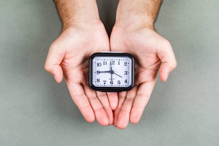 time management clock ticking concept with clock gray background top view hands holding clock horizontal image